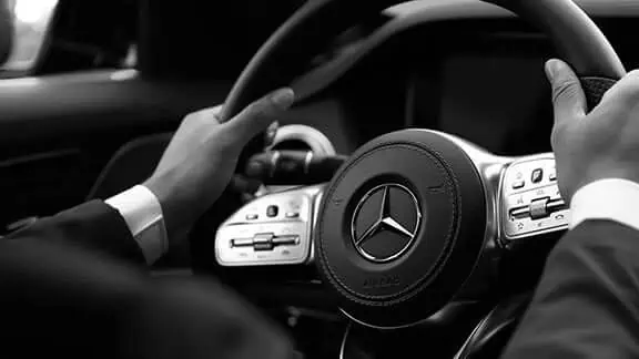 A man in a suit is driving a mercedes benz.