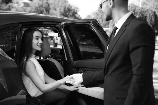 Black and white photo of a man and woman shaking hands in front of a car.