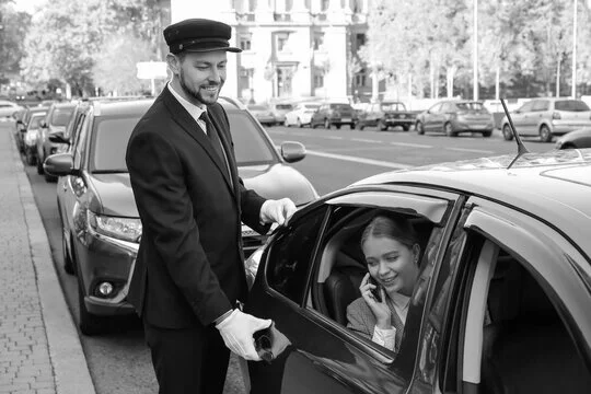 A black and white photo of a man in a suit standing next to a woman in a car.