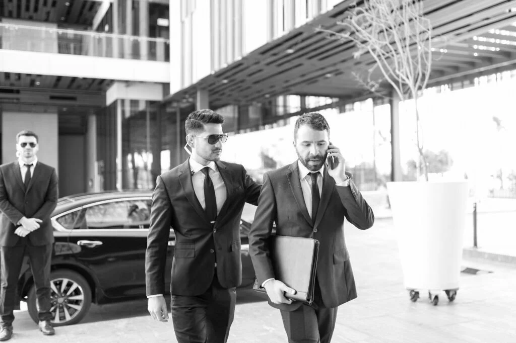 Black and white photo of businessmen walking in front of a car.