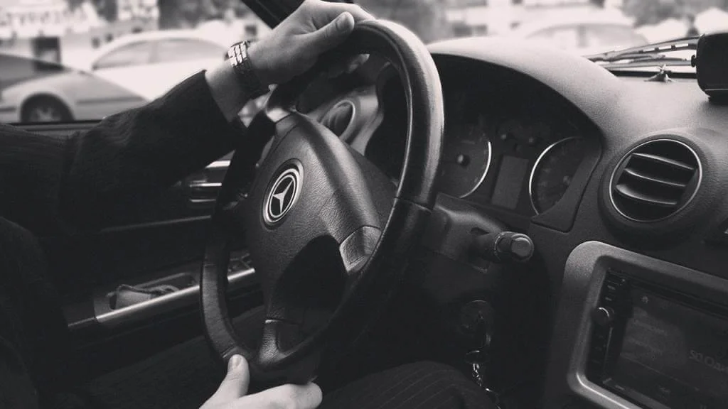 A man driving a car with his hands on the steering wheel.